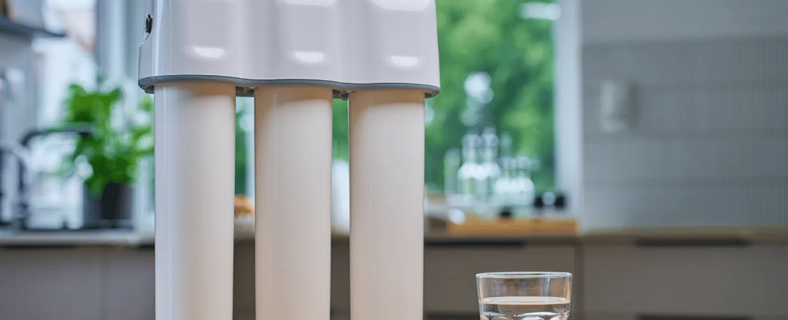 White three-stage water filter system on kitchen counter with glass of clean water beside it