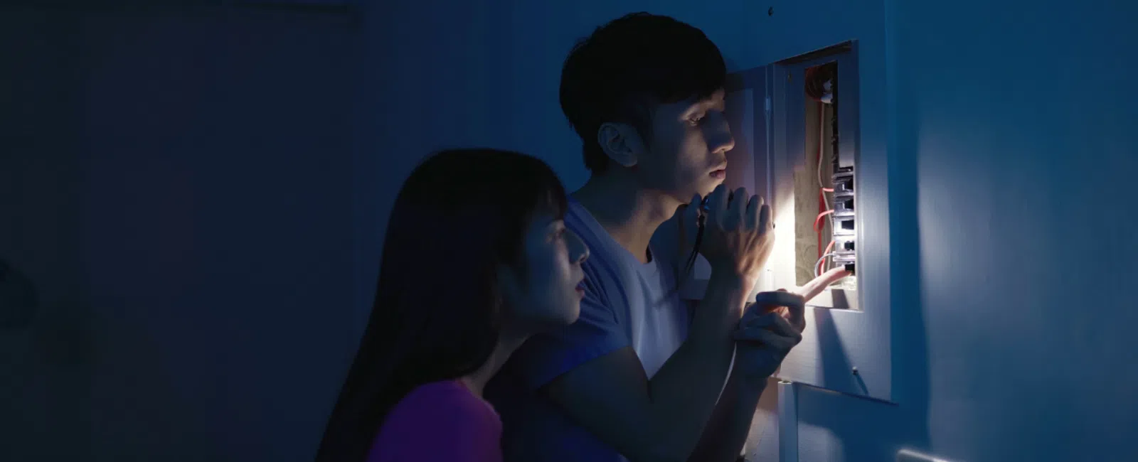 Couple inspecting electrical panel with flashlight in dark room during power outage or repair.