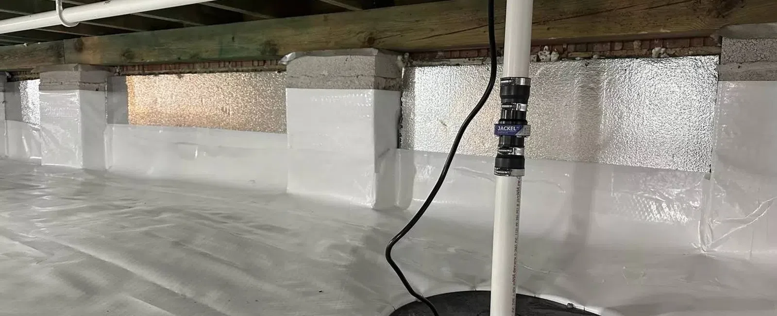 Clean, bright crawl space with white vapor barrier and installed sump pump system for moisture control.