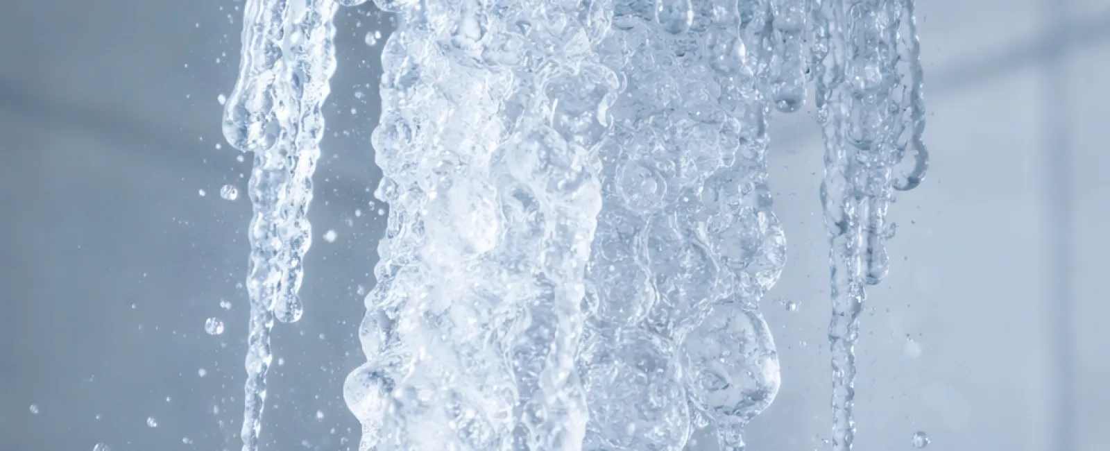 Close-up of water flowing from a silver showerhead against a tiled bathroom wall, creating bubbly streams.