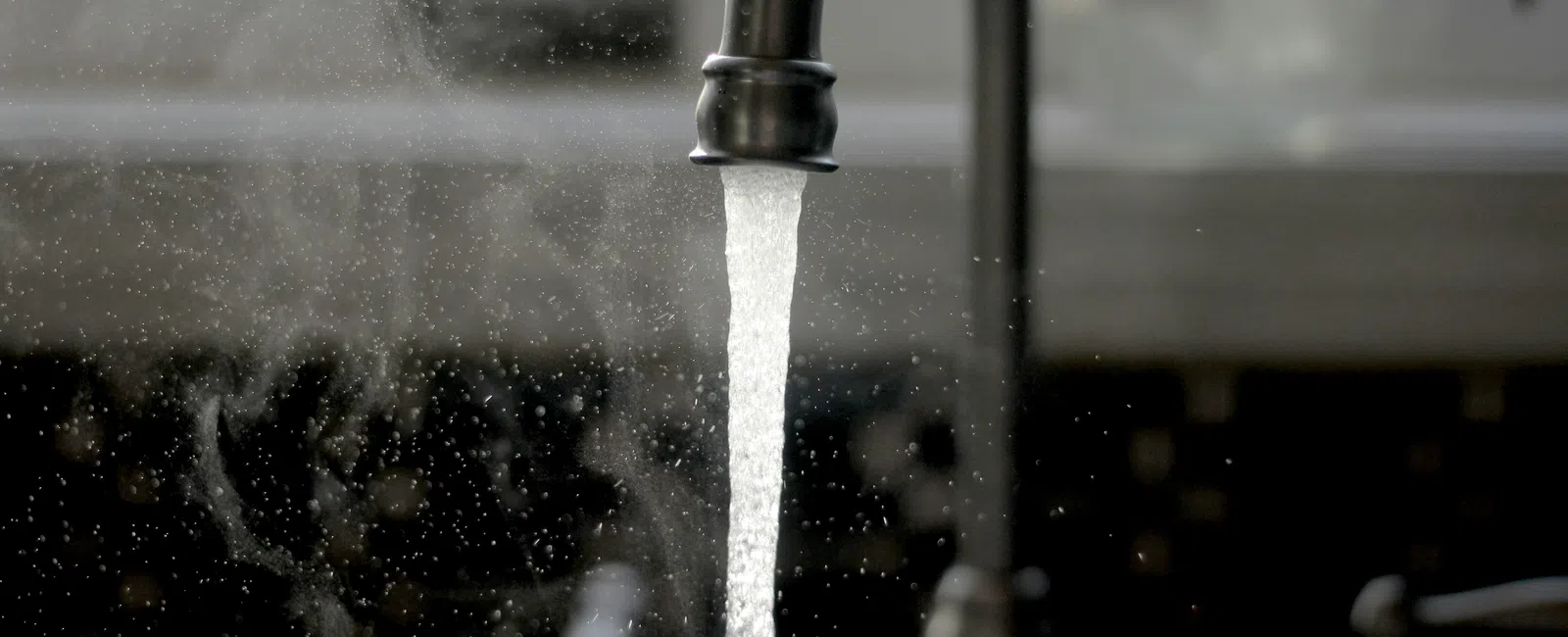 Steam rises from hot water flowing from a black kitchen faucet against a blurred dark background.