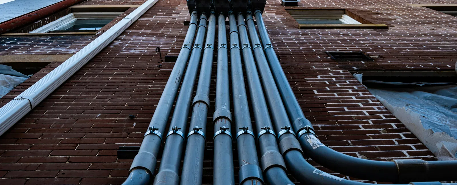 Low-angle view of metal electrical conduits mounted on a brick building exterior with clear blue sky above.