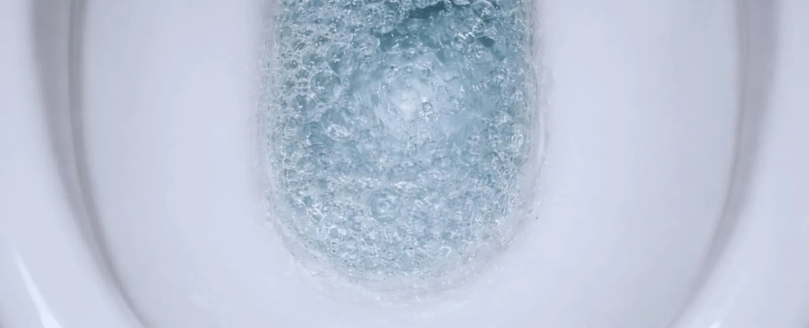 Close-up of water swirling and bubbles inside a flushing white ceramic toilet bowl.