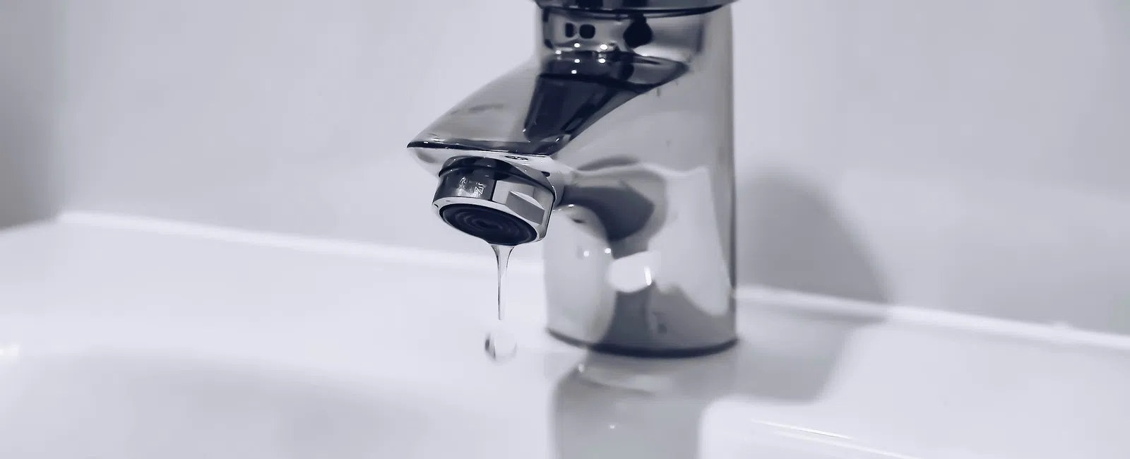 Close-up of a silver faucet dripping water over a white sink with a simple background.