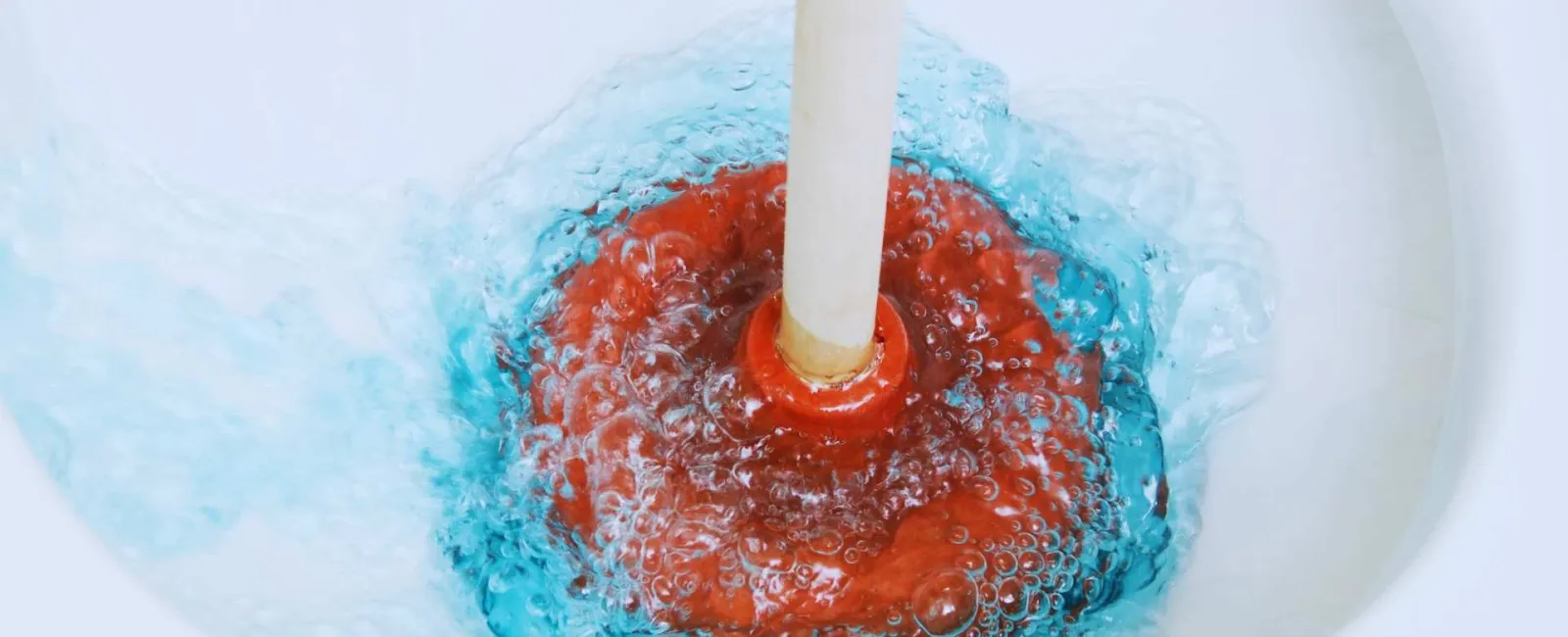Red plunger creating bubbles as it unclogs blue water in a white sink drain.