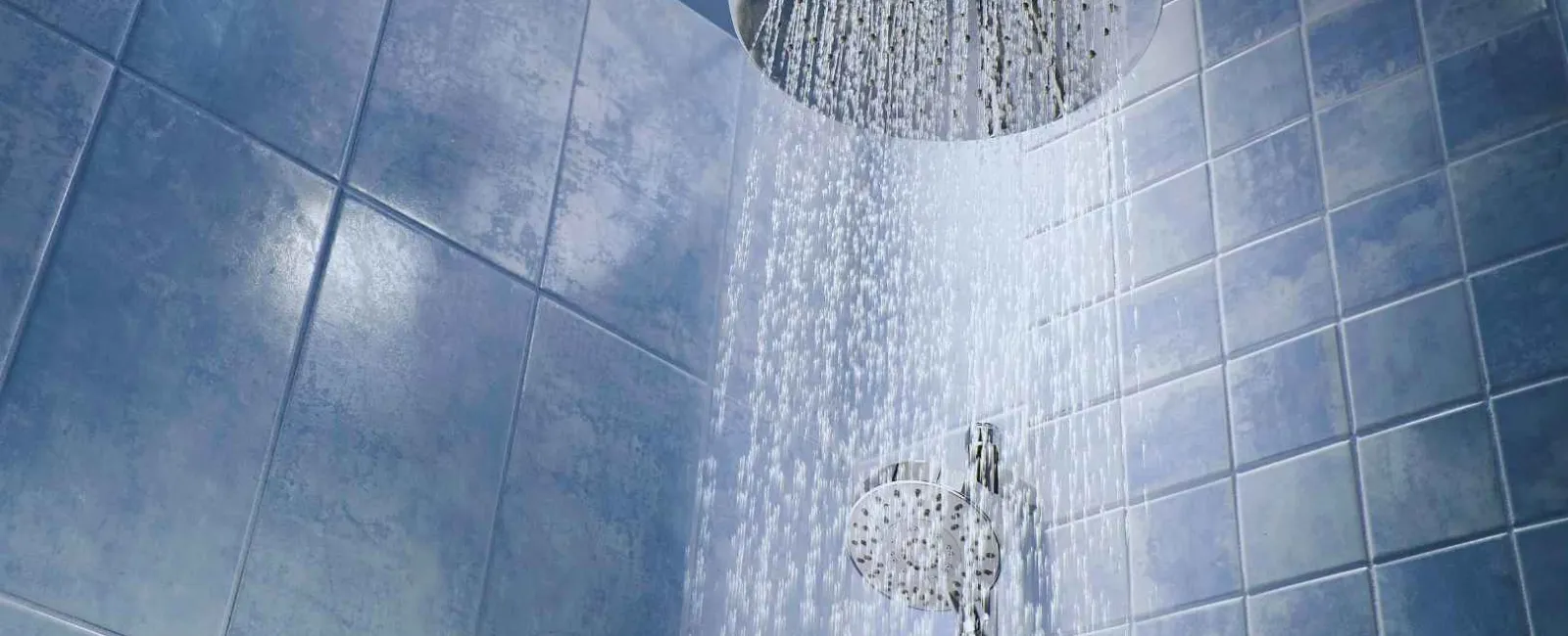 Modern chrome rainfall showerhead with water flowing in a tiled blue bathroom.