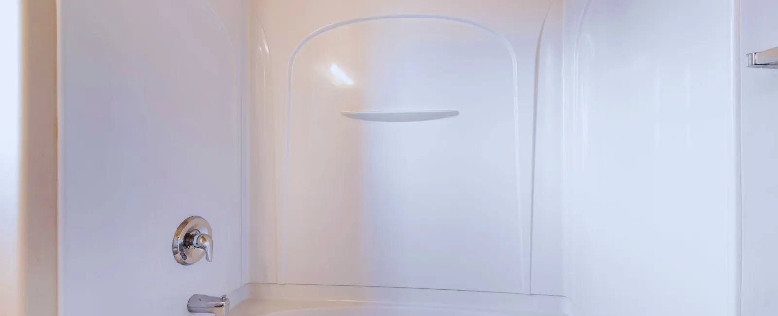 Clean white bathtub with surrounding shower walls and silver faucet and showerhead in beige bathroom.