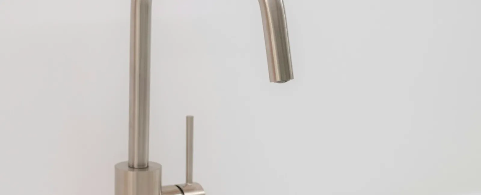 Modern stainless steel kitchen faucet over a clean white sink with minimalist design.