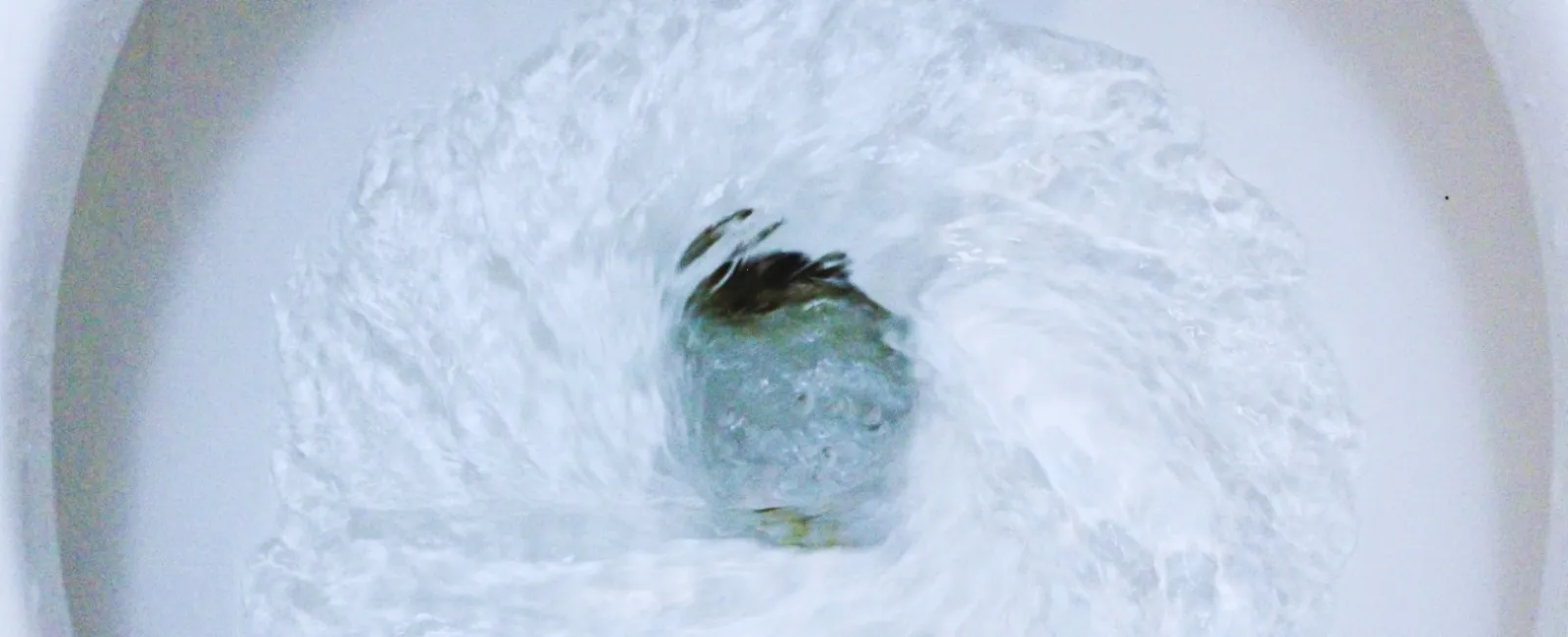 Water swirling and draining rapidly in a white toilet bowl during flushing in a bright setting