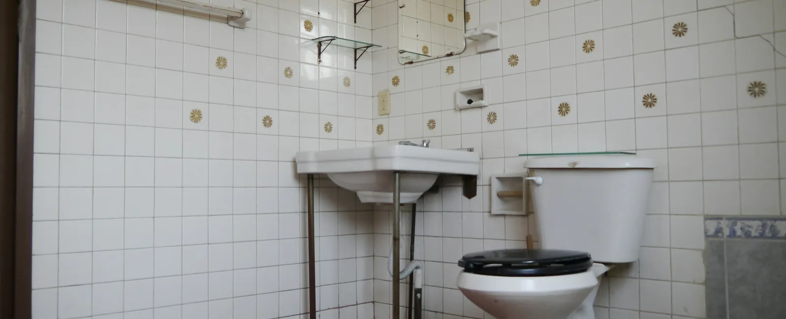 Small bathroom with white tiles decorated with yellow flower patterns, a white sink, and a toilet with a black seat.