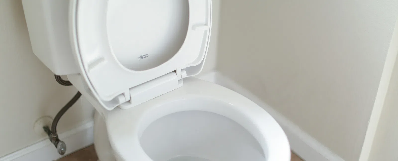 Clean white toilet with open lid in a beige tiled bathroom corner near white walls and baseboard.