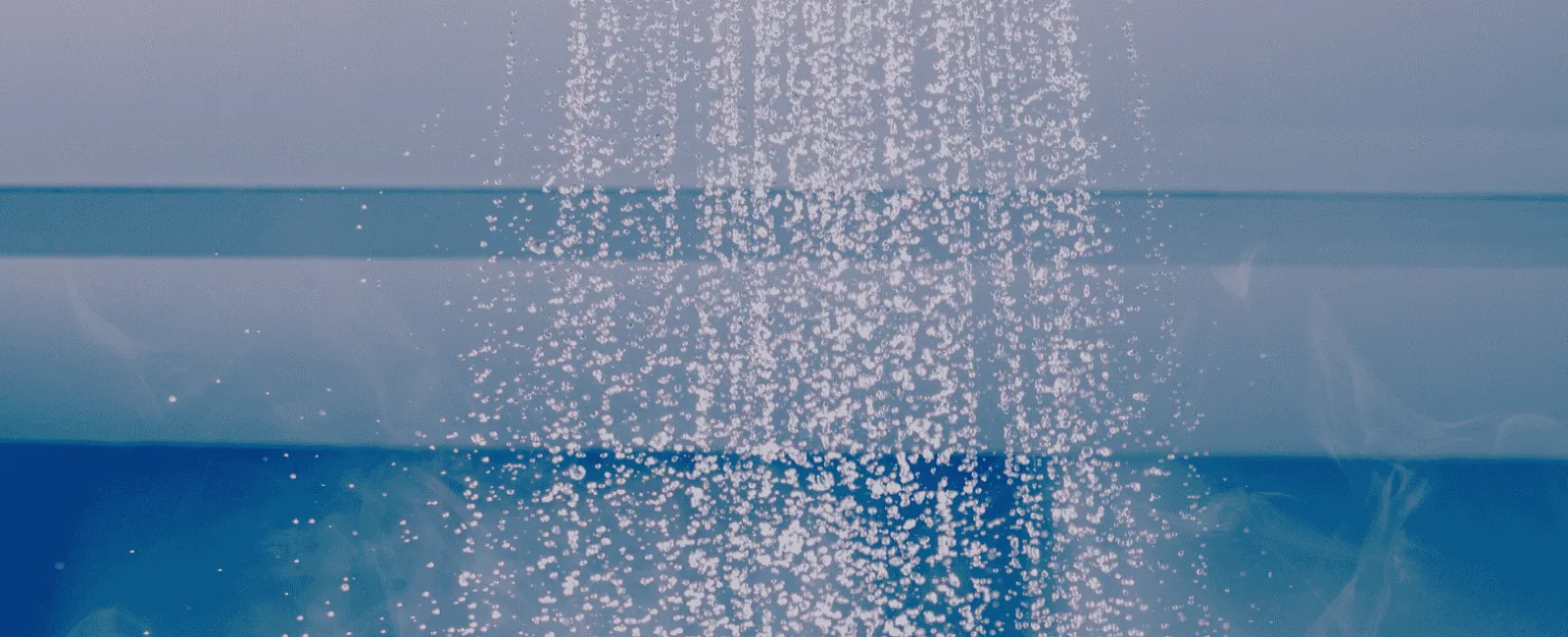 Steam rising from hot water pouring from a round ceiling showerhead against a blue background