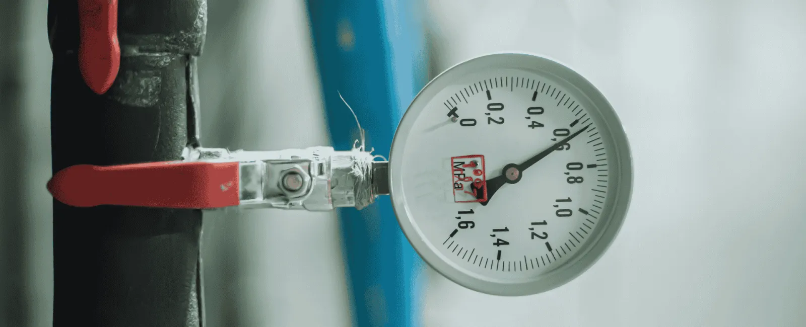 Close-up of a pressure gauge attached to a black pipe with a red valve handle in a mechanical setting.