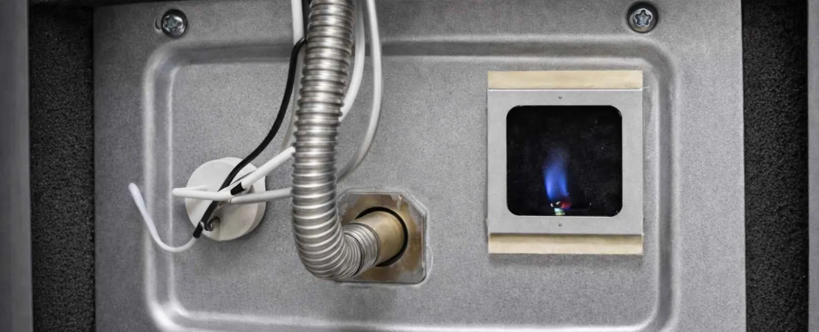 Close-up of a gas furnace burner igniting with blue flame inside metal housing and connected wires.
