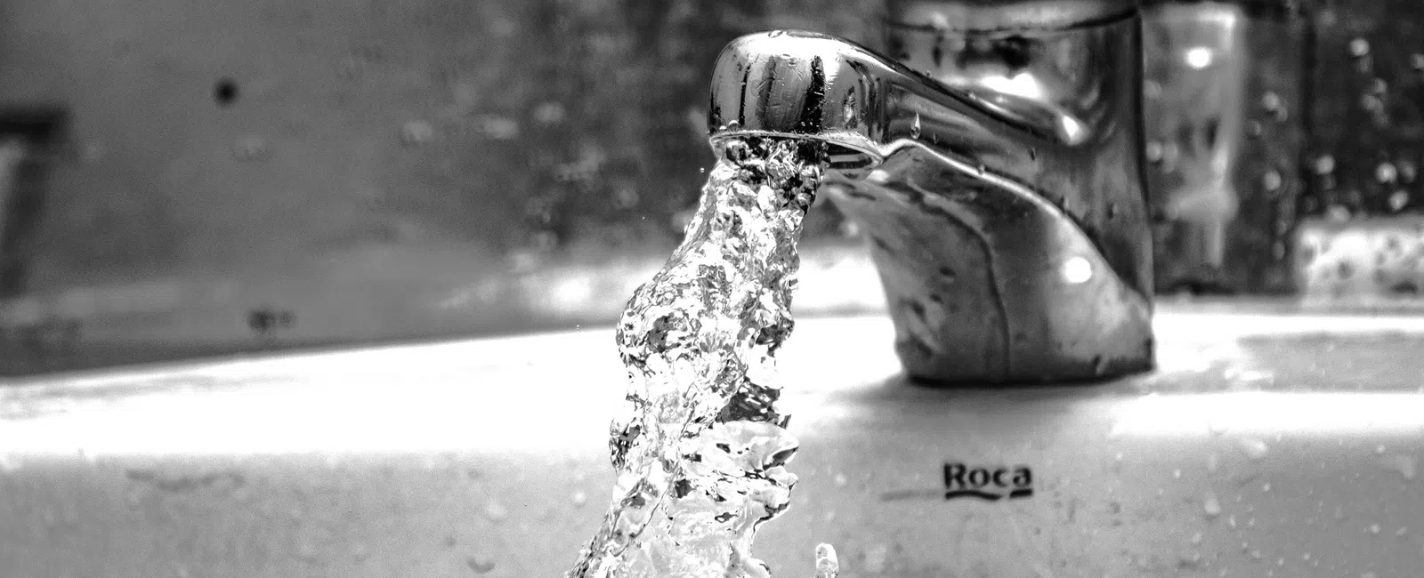 Close-up of water flowing from a chrome faucet into a white sink in black and white.