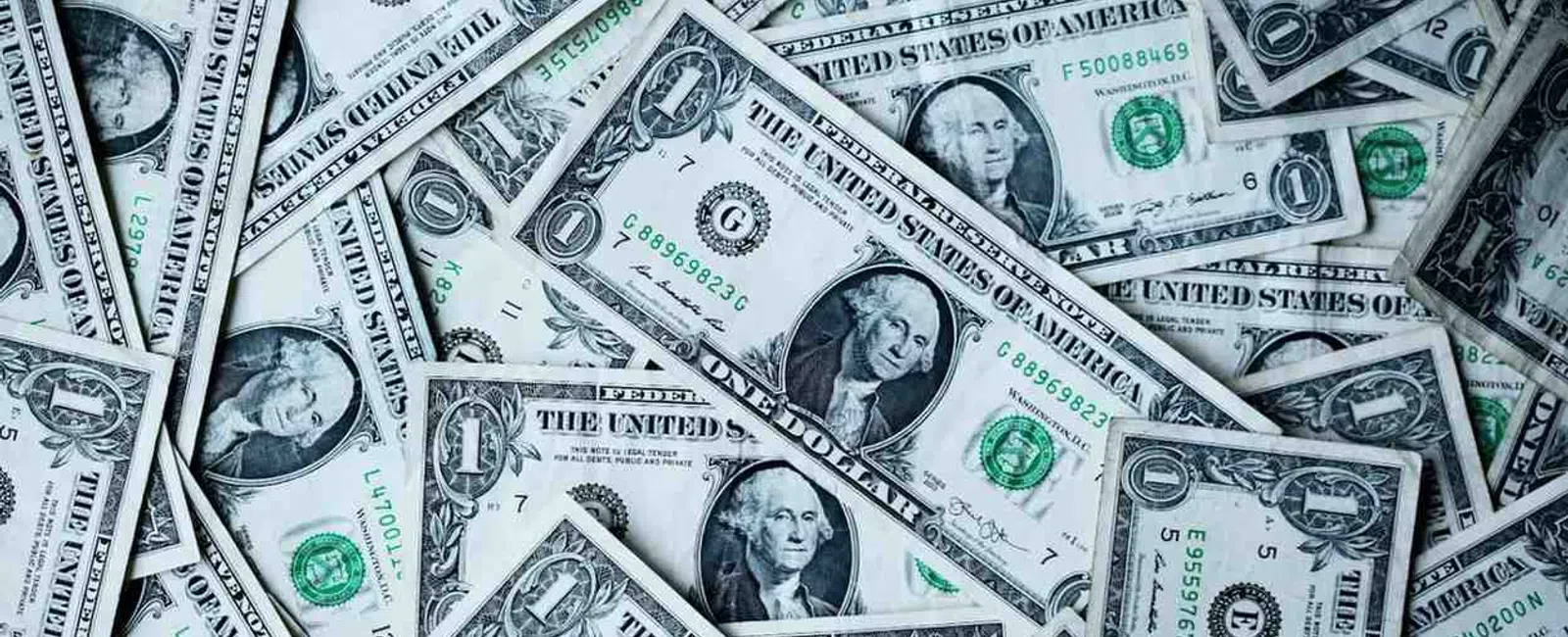 Pile of scattered one dollar bills showing George Washington's portrait and green treasury seals.