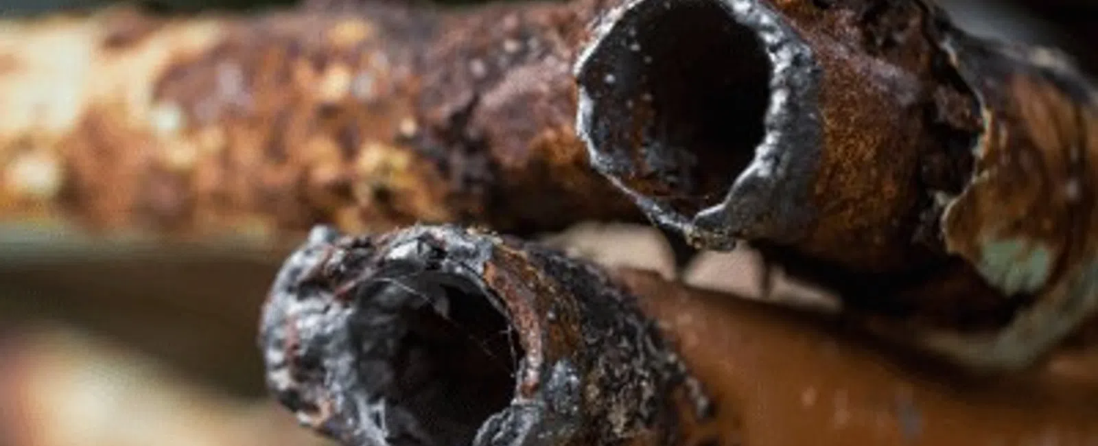 Close-up of severely rusted metal pipes with corroded edges and flaky surface texture in warm light.