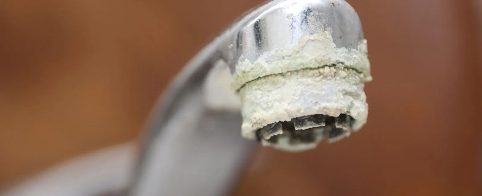 Close-up of a metal faucet with white mineral deposits and limescale buildup around the spout tip.