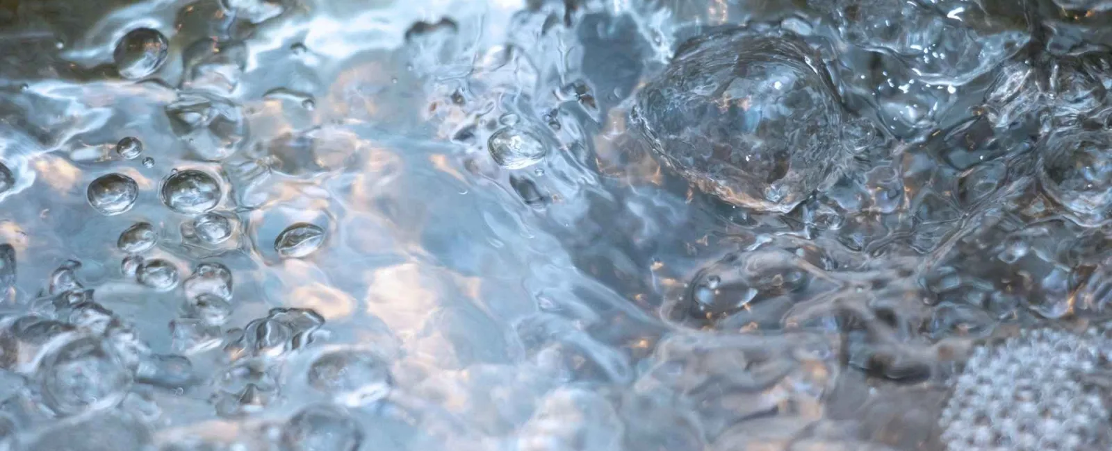 Close-up of bubbling, boiling water with rising steam and water droplets in motion.