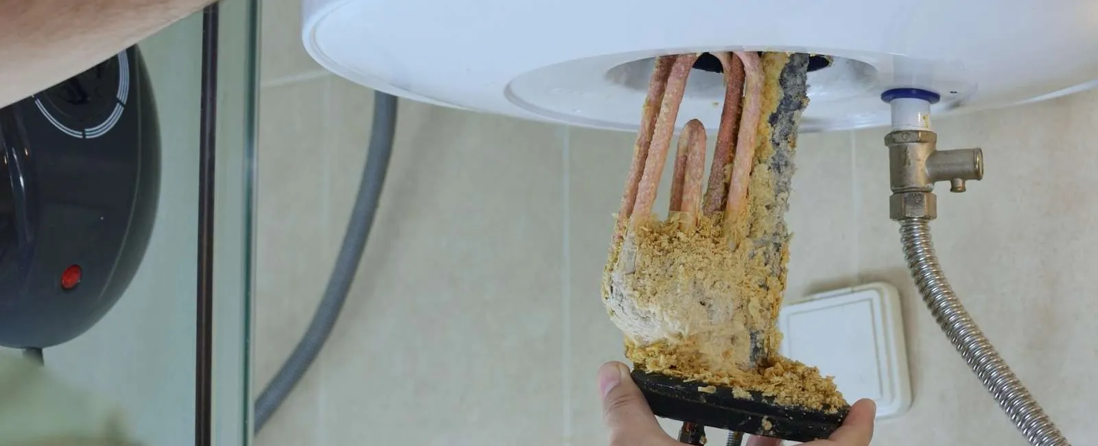 Hands removing a heavily corroded heating element from a water heater for maintenance or replacement.