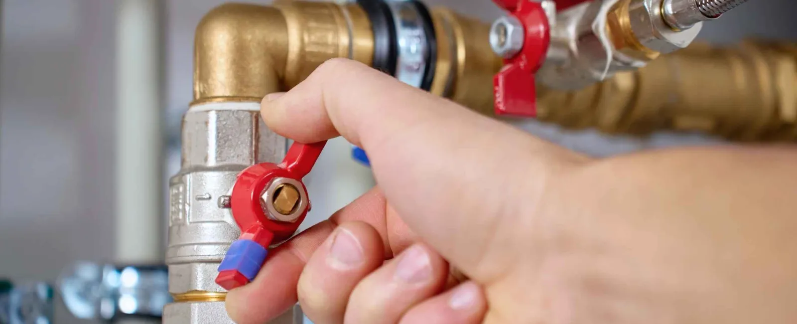 Close-up of hand turning a red valve on a brass plumbing pipe with metal fittings and connectors