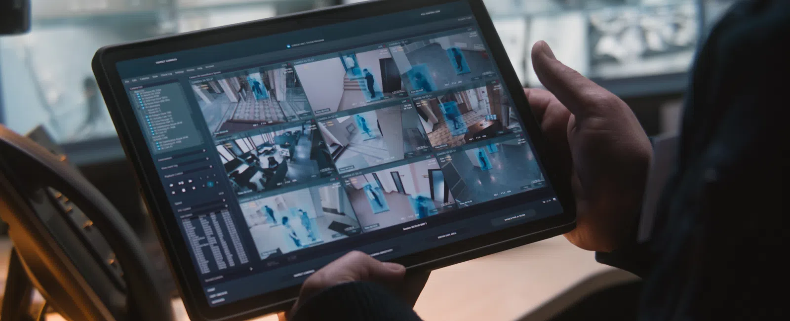 Person monitoring multiple security camera feeds on a tablet in a dimly lit control room.