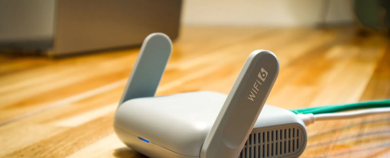 White WiFi 6 router with dual antennas on a wooden table, connected by a green Ethernet cable.