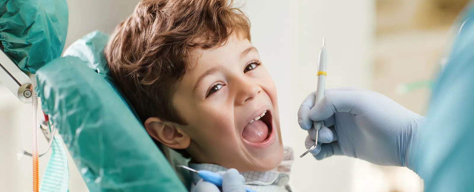 Young boy sitting in dental chair with mouth open while dentist prepares to examine his teeth