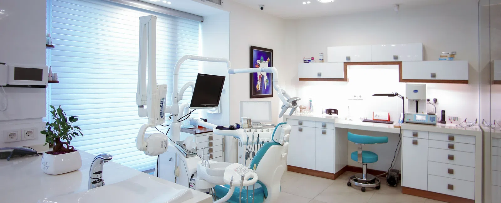 Bright modern dental office with dental chair, equipment, sink, and white cabinets under soft lighting.