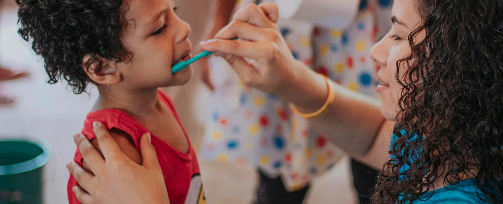 Woman helping young child brush teeth with a toothbrush in an indoor setting, close interaction shown