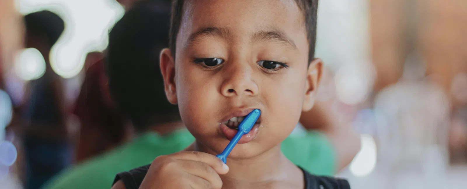 Young boy brushing his teeth with a blue toothbrush indoors, focusing on oral hygiene practice.