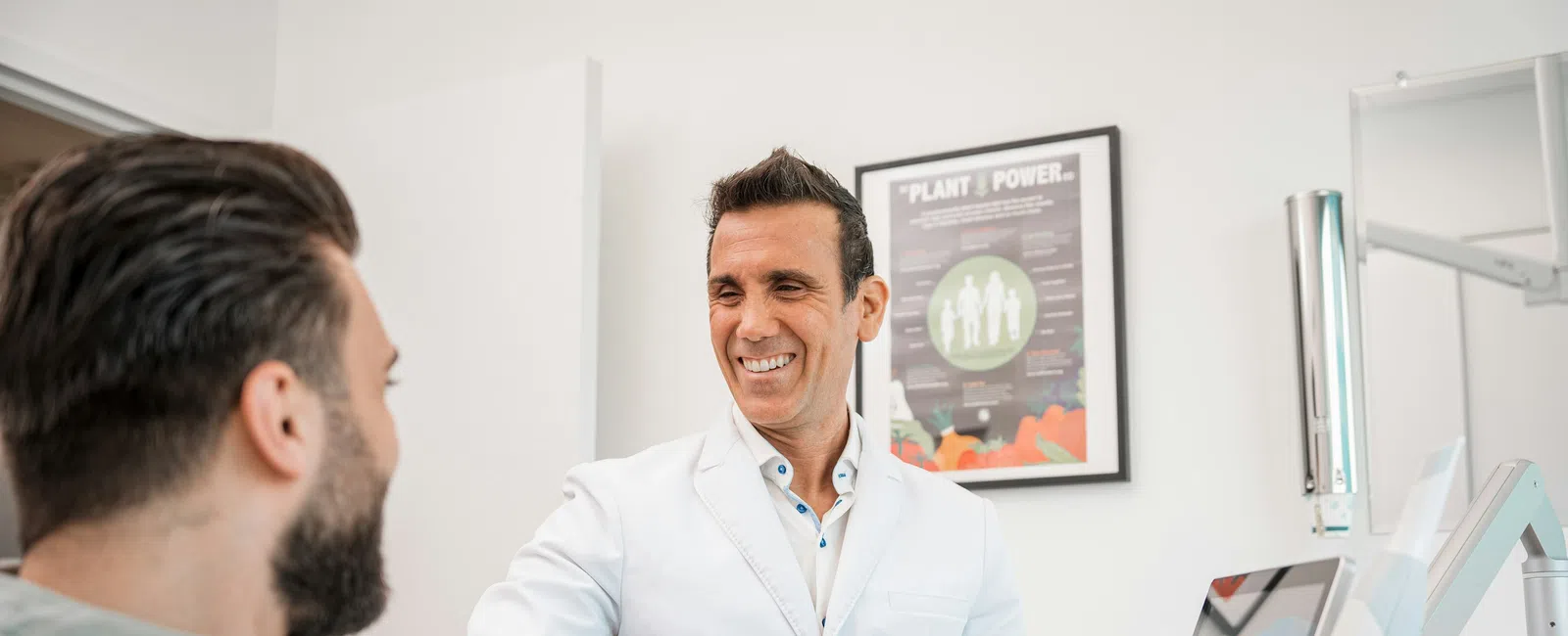 Smiling male dentist in white coat talking to a male patient in a modern dental office with equipment.