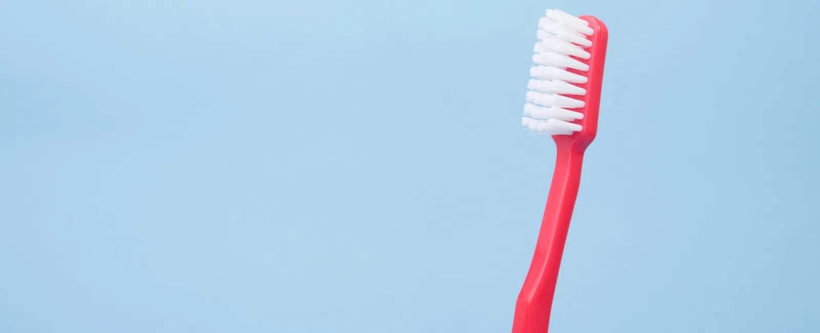 Red toothbrush with white bristles on a light blue background for dental hygiene.