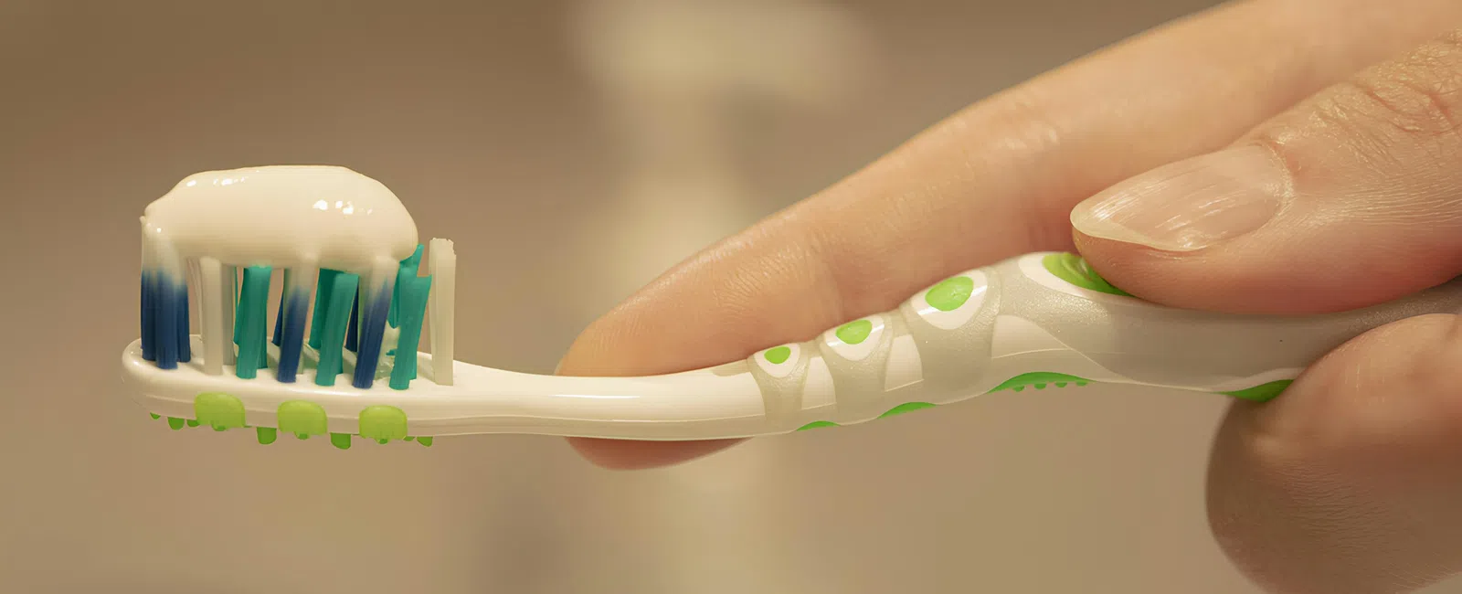 Hand holding a white and green toothbrush with blue bristles and a dollop of white toothpaste.