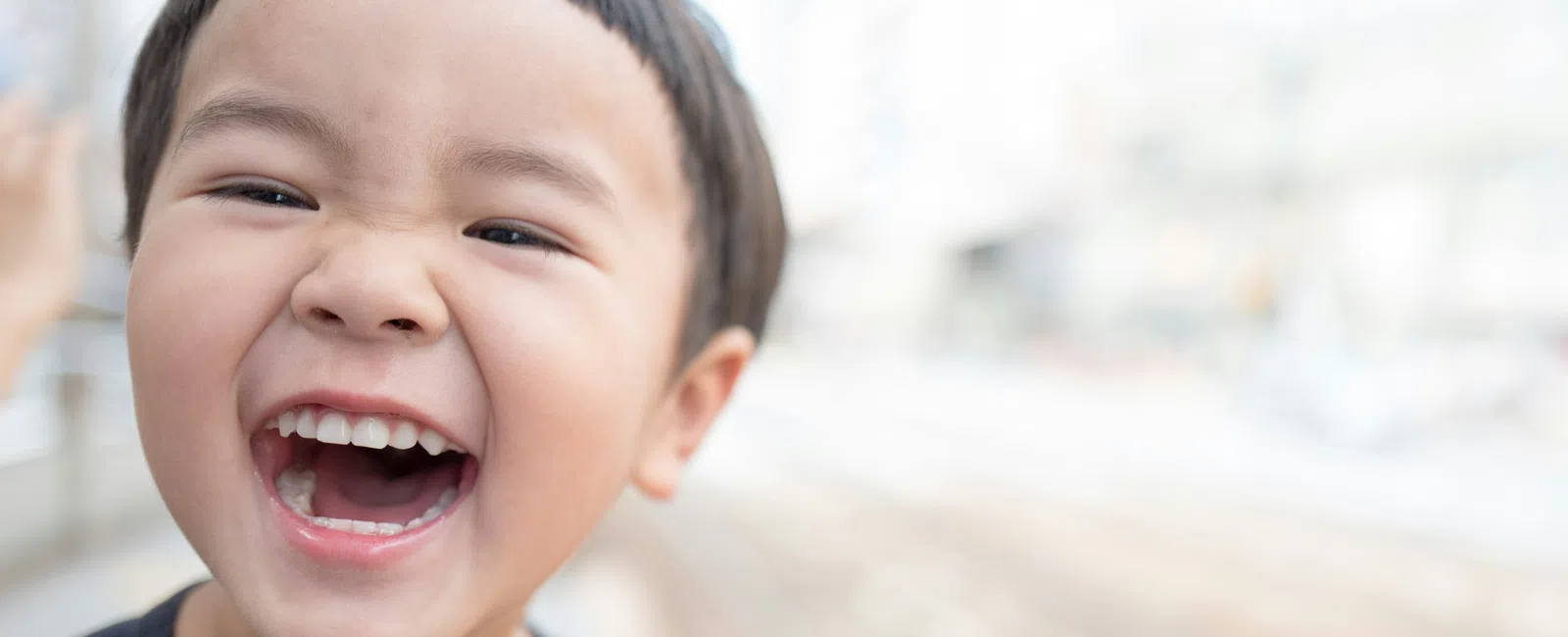 Close-up of a happy young boy laughing outdoors with a blurred urban background.