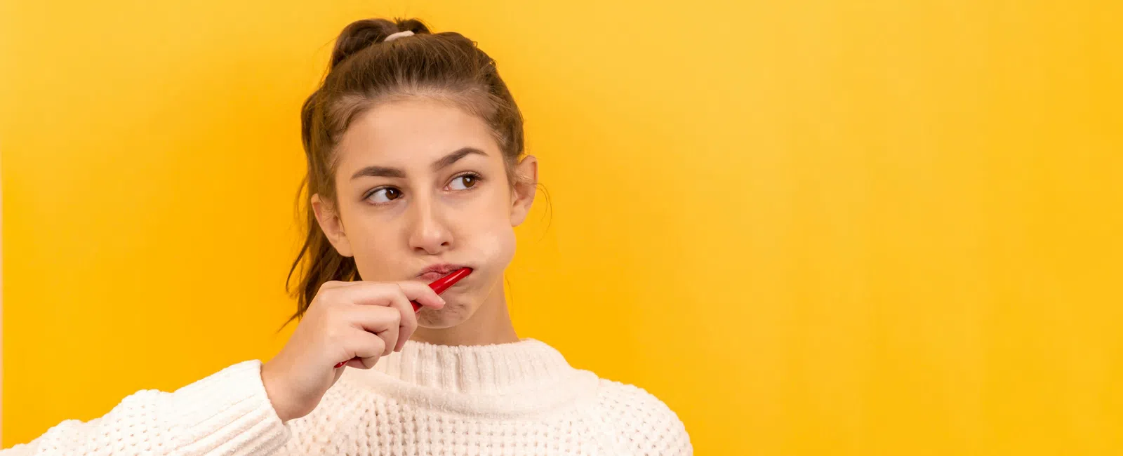 Young woman brushing her teeth with red toothbrush against bright yellow background