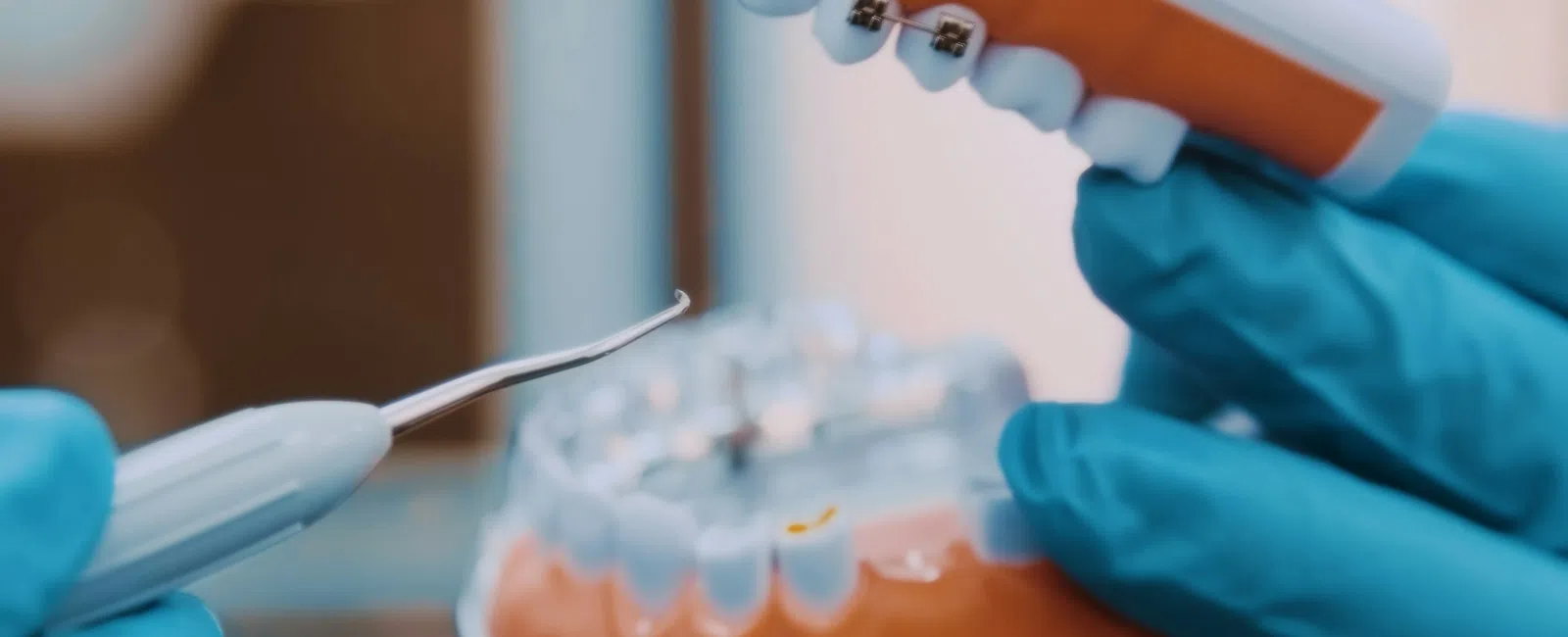 Dental model with braces held by gloved hands and dental tool demonstrating orthodontic care.