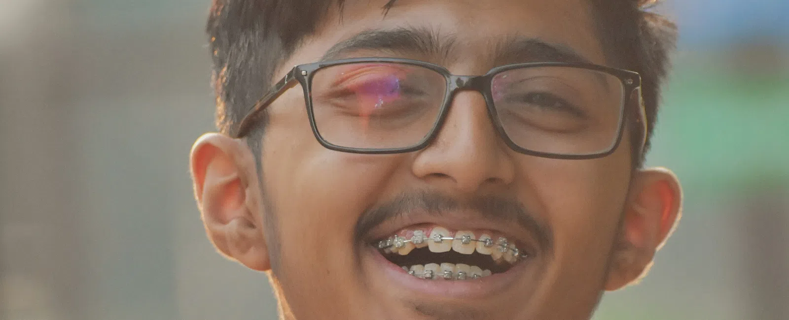 Teen boy with braces and glasses smiling in an outdoor setting wearing a red shirt.