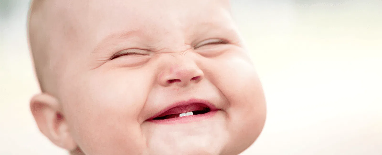 Close-up of smiling baby with eyes closed showing two front teeth and joyful expression