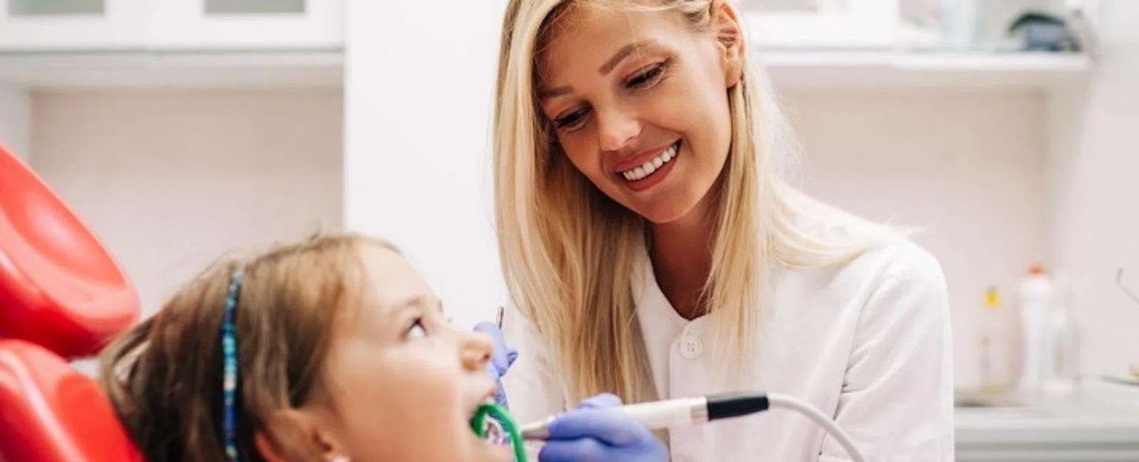 Smiling female dentist treating young girl patient using dental tools in modern clinic