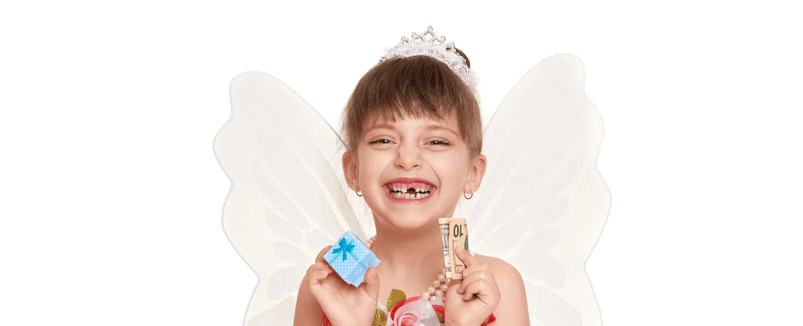 Smiling girl with missing teeth wearing fairy wings and holding a small gift box and money against white background