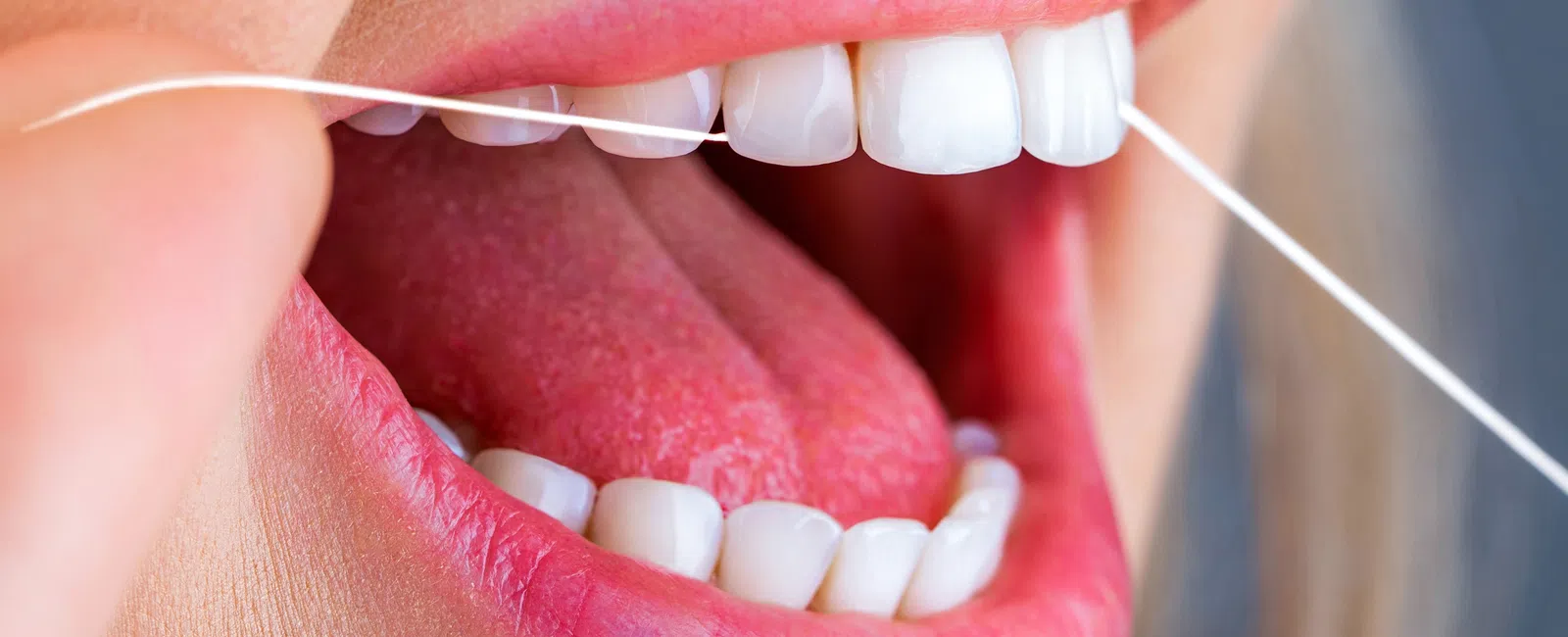 Close-up of a person flossing their teeth showing lips, tongue, white teeth, and dental floss string.