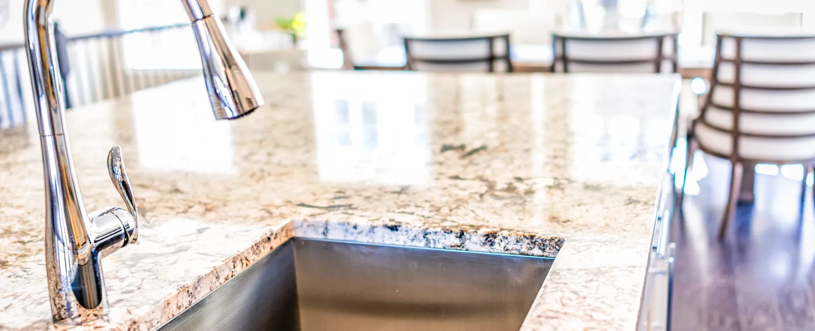 Close-up of a sleek kitchen sink integrated into a polished granite countertop with modern furnishings.