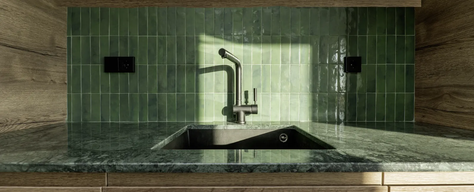 Modern kitchen sink with green tiled backsplash and wooden cabinetry under natural light.