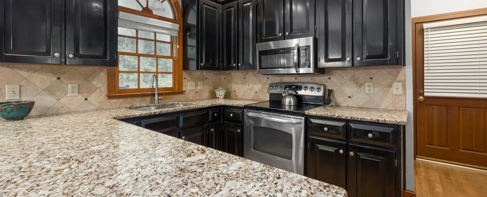 Modern kitchen with black cabinets, granite countertops, stainless steel appliances, and wood trim accents