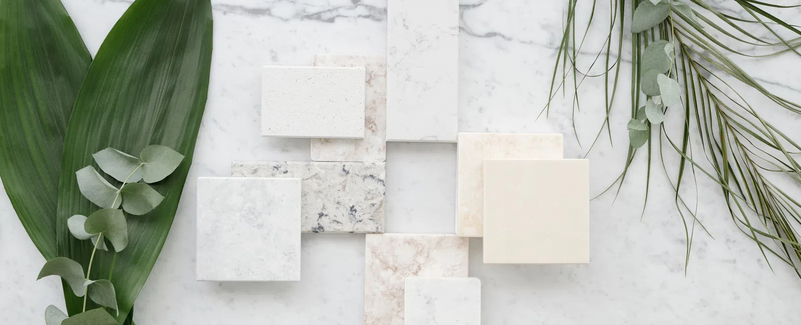 Various marble and stone tile samples arranged on a white marble surface with green leaves on sides