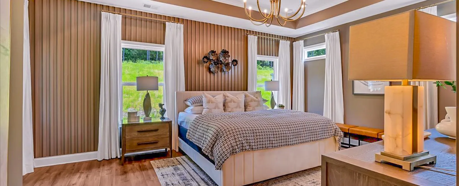 Spacious modern bedroom with beige tones, large bed, wooden nightstands, floor lamp, and windows with white curtains.