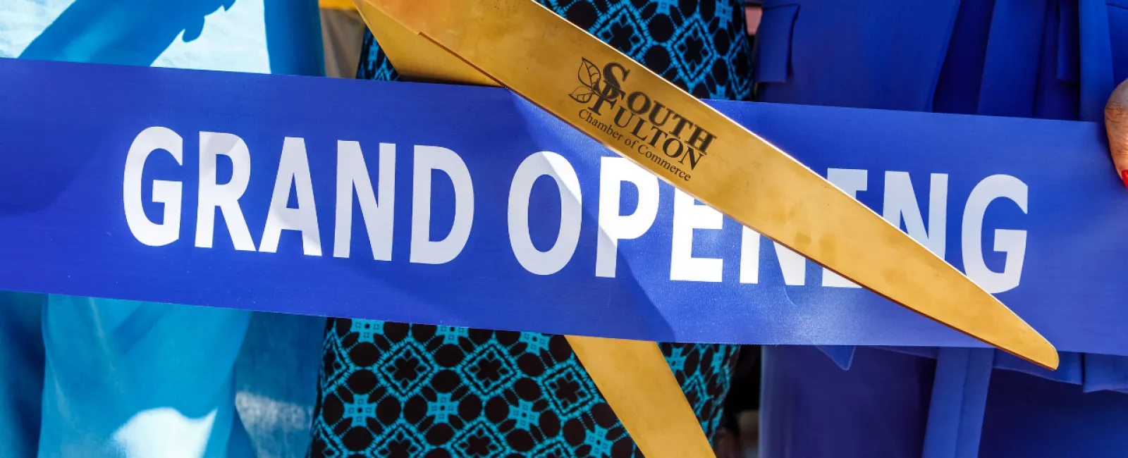 a person cutting a grand opening ribbon with golden scissors