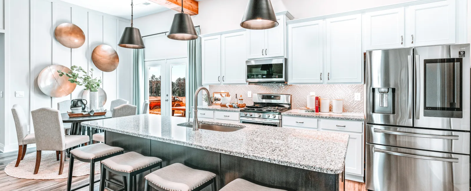 Bright modern kitchen with white cabinets, granite island, stainless appliances, wooden beams, and black pendant lights