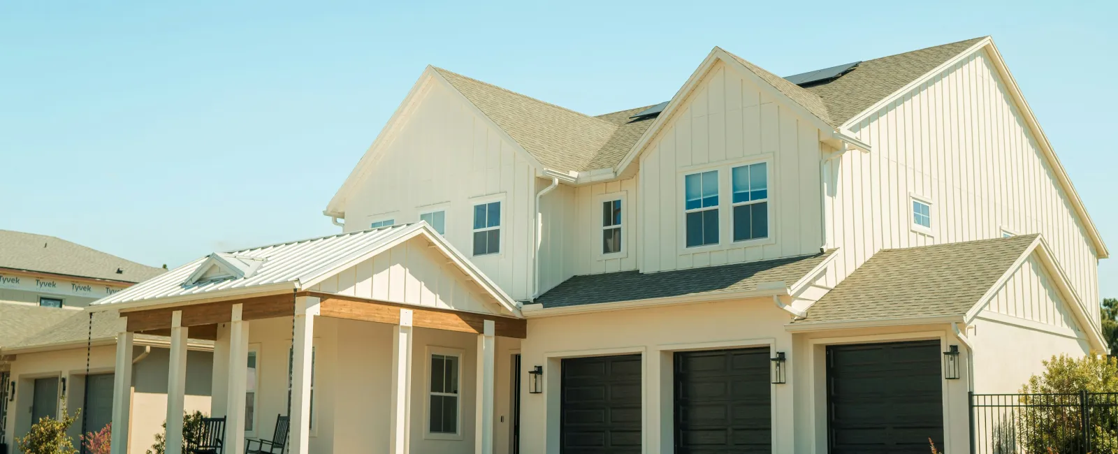 Modern two-story white house with black garage doors, front porch, and neatly landscaped lawn under clear blue sky.